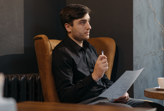 Man in Black Long Sleeve Shirt Sitting on a Chair While Holding a Paper